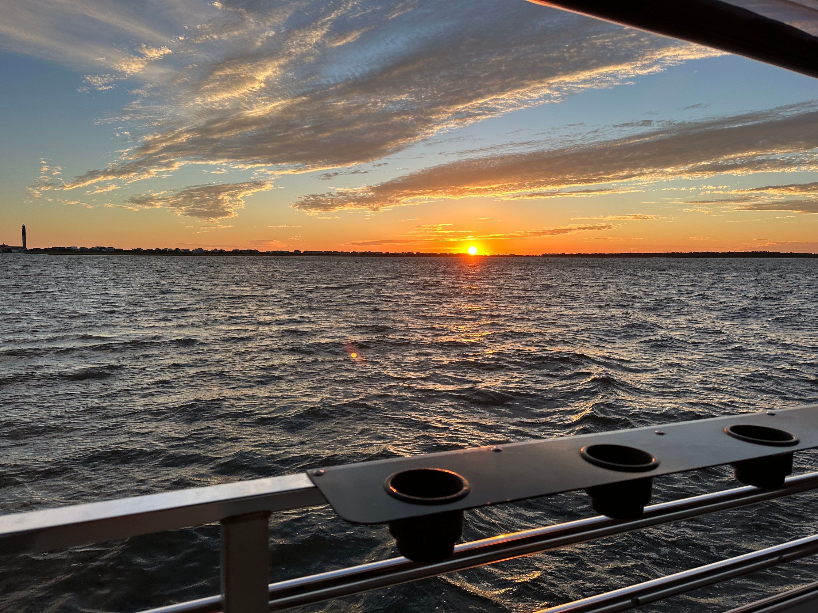 Sunset over a calm sea with clouds and railing in the foreground.